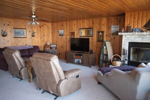 A wooden-paneled room with a fireplace, a television, and two recliner chairs.