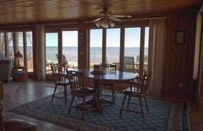Un coin repas avec une table et des chaises, de grandes fenêtres donnant sur la mer et un ventilateur de plafond.