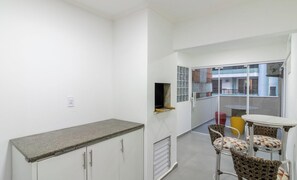 A small kitchenette with a countertop and cabinets, a sliding glass door leading to an outdoor area with a table and chairs. - Apts in a Building 180m From the Beach in Balneario Camboriu - Rajs (Balneário Camboriú)