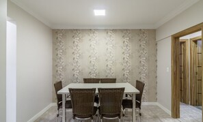 A dining area with a table and chairs, a floral wallpaper, and a wooden door. - Apts in a Building 180m From the Beach in Balneario Camboriu - Rajs (Balneário Camboriú)