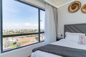 Een slaapkamer met een groot raam, een bed met wit beddengoed, een grijs hoofdeinde en twee decoratieve borden aan de muur.