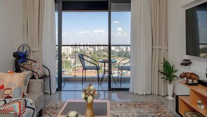 A modern living room with a sofa, a coffee table, a TV, and a balcony with a city view. - Luxurious apartment near mall and Carrefour, giving a cozy and homely vibe (Nairobi)