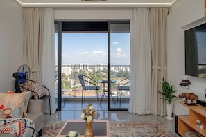 A modern living room with a sofa, a coffee table, a TV, and a balcony with a city view. - Luxurious apartment near mall and Carrefour, giving a cozy and homely vibe (Nairobi)