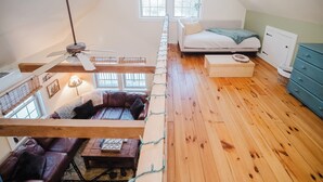 Ein Schlafzimmer im Loft-Stil mit geneigter Decke, Holzboden, einem weißen Bett, einer blauen Kommode und einem Deckenventilator.