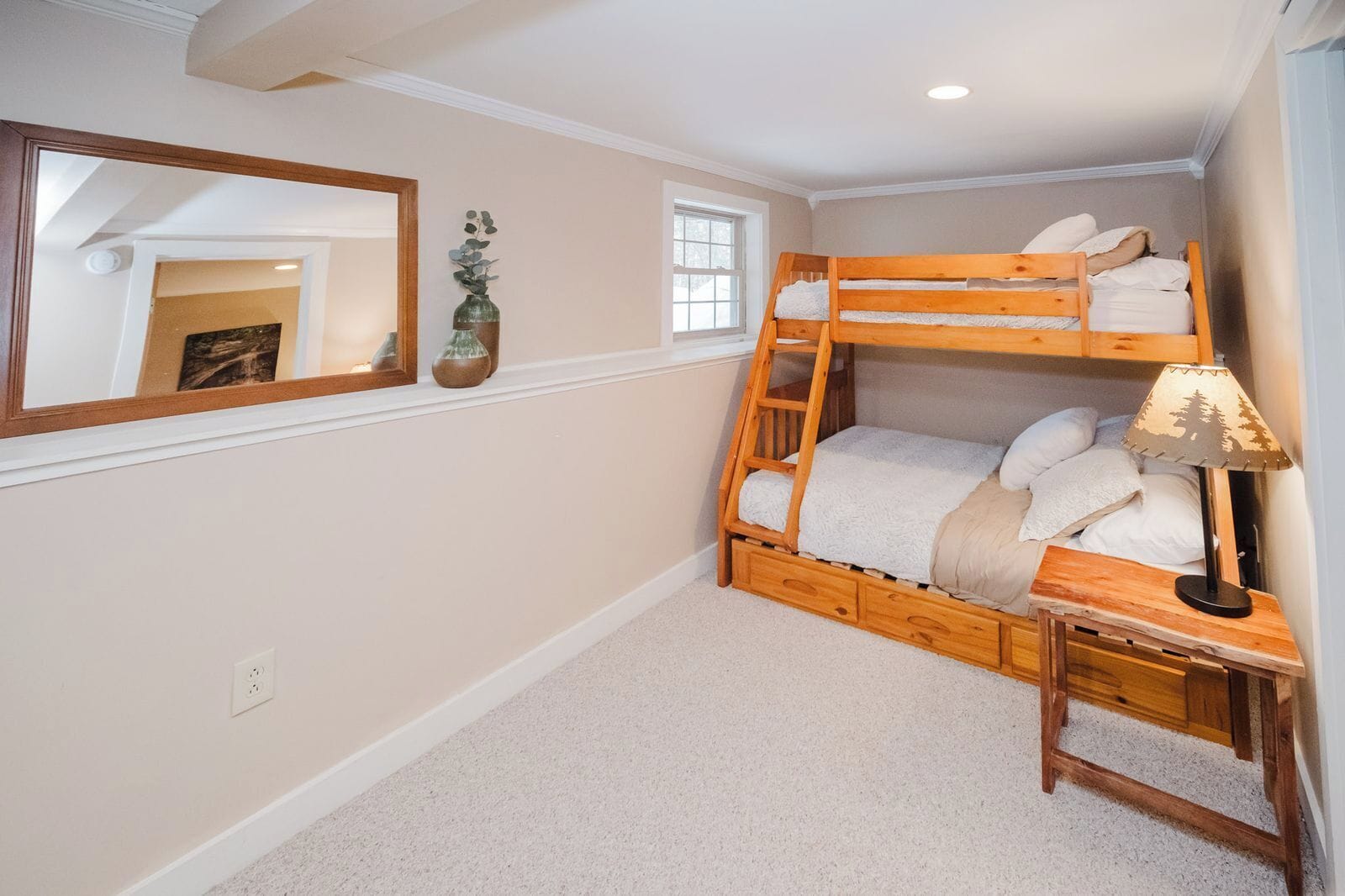 A bunk bed with a ladder, a bedside table with a lamp, a mirror, and a small window.