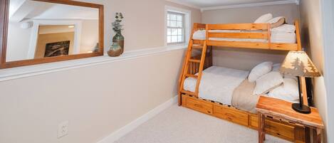 A bunk bed with a ladder, a bedside table with a lamp, a mirror, and a small window.