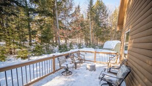 Eine Holzterrasse mit Gartenmöbeln, umgeben von schneebedeckten Bäumen.