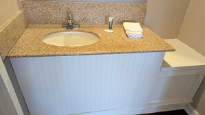 A bathroom with a granite countertop sink, a white vanity, and a dark wooden floor. - Exceed Inn Indianapolis Airport South (Indianapolis)