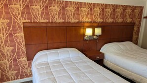 A hotel room with two beds, a wooden headboard, patterned wallpaper, and wall-mounted lamps. - Exceed Inn Indianapolis Airport South (Indianapolis)