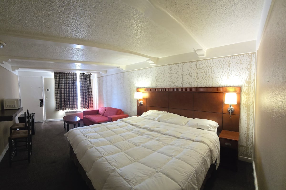 A hotel room with a large bed, a TV, a microwave, a small table, a red chair, and a sofa.