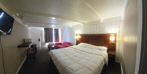 Camera d'albergo con un letto grande, una TV, un forno a microonde, un tavolino, una poltrona rossa e un divano.