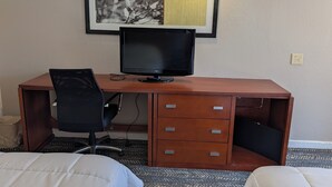 A hotel room with a wooden desk, a black office chair, a flat-screen TV, and a framed picture on the wall. - Exceed Inn Indianapolis Airport South (Indianapolis)