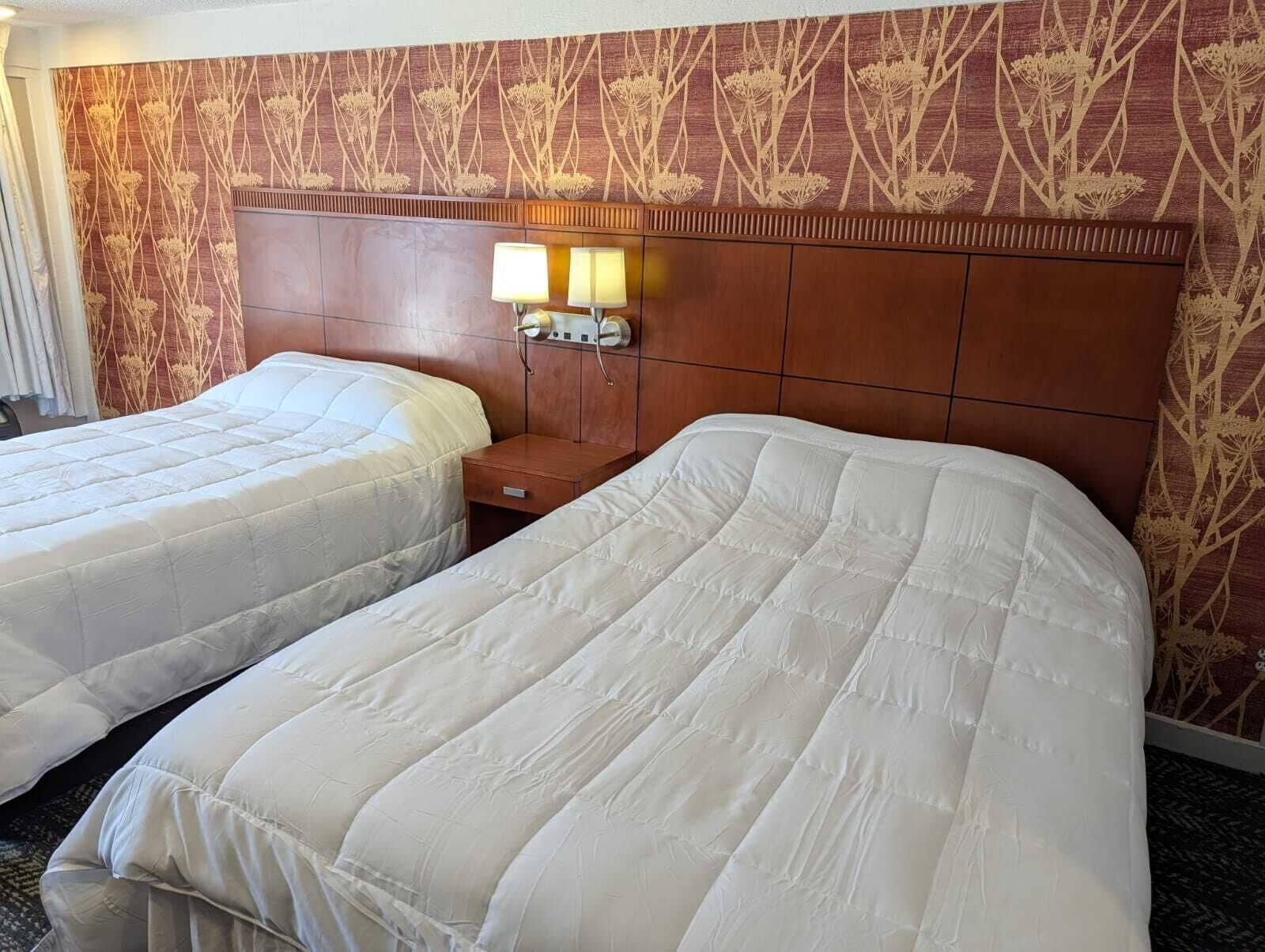 Habitación de hotel con dos camas, cabecero de madera y pared con estampado floral.