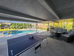 Ein Poolbereich im Freien mit Tischtennisplatte, Liegestühlen und Grill.