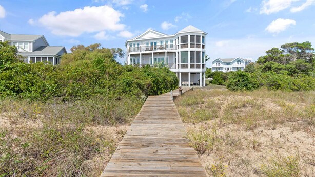 Una passerella di legno conduce a una grande casa bianca a più piani, con numerosi balconi e ampie finestre.