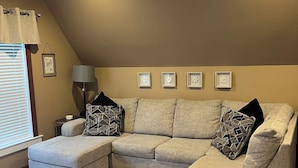 A modern living room with a sectional sofa, a side table, a lamp, and a patterned rug. - The Fannie Historic Apartment (Eau Claire)