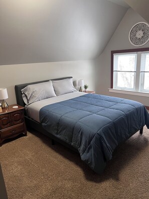 A bedroom with a bed, nightstand, lamp, and a window with blinds.