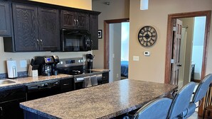 A modern kitchen with dark wood cabinets, a granite countertop, stainless steel appliances, and a bar area with stools. - The Fannie Historic Apartment (Eau Claire)