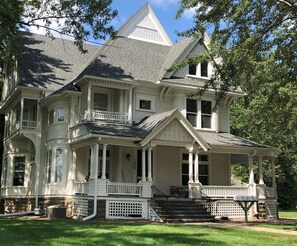A large, two-story house with a wrap-around porch, multiple windows, and a steeply pitched roof. - The Fannie Historic Apartment (Eau Claire)