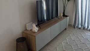 Un salon moderne avec un téléviseur à écran plat posé sur une console en bois, un objet décoratif blanc, un panier en osier et une plante en pot.