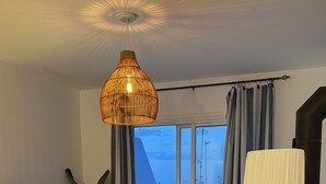 Un salon moderne avec un canapé, un téléviseur, un luminaire suspendu et une vue sur l’extérieur grâce à de grandes portes coulissantes.