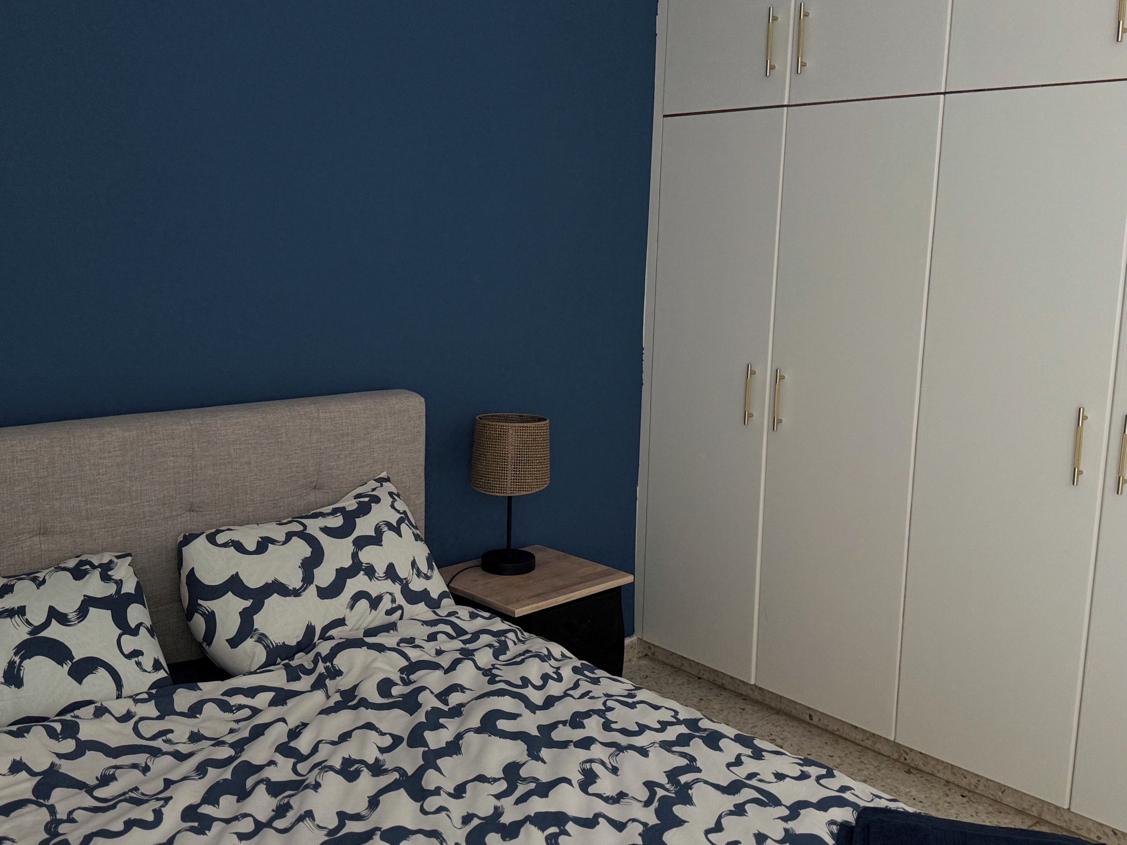 A bedroom with a bed, a nightstand, a lamp, and a wardrobe.