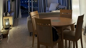 Un salon moderne avec un coin repas, comprenant un canapé, une table à manger avec des chaises et deux lampes suspendues.