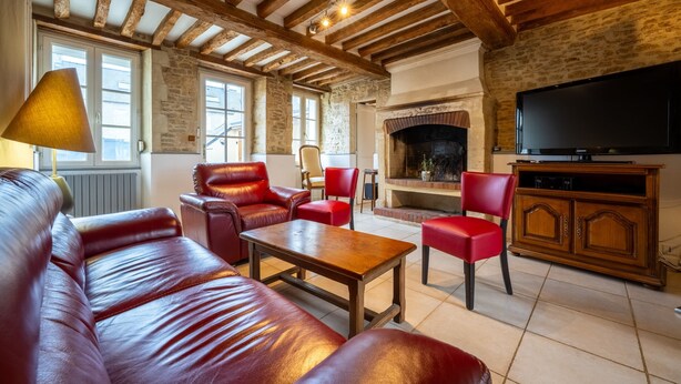 A cozy living room with a leather sofa, red chairs, a wooden coffee table, a fireplace, and a television. - Cyrano & Roxane - 1 km de la plage (Ver-sur-Mer)
