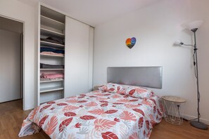 A bedroom with a bed, a wardrobe, a bedside table, and a floor lamp. - Le Petit Logis du Stade de France (Saint Denis)