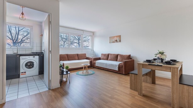 En moderne lejlighed med vaskefaciliteter, to sofaer, et spisebord og store vinduer.