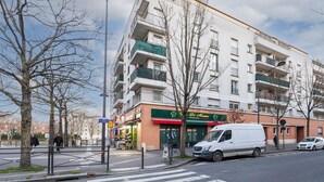 En bygning med flere etager og balkoner, en restaurant i stueetagen, og en hvid varevogn parkeret på gaden.