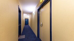 Et hotel med et tæppe belagt gulv, døre på begge sider samt en lampe over døren til højre.
