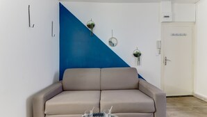 Ein Zimmer mit einem beigefarbenen Sofa, einem Glastisch mit zwei Gläsern und einer blau gestrichenen Wand.