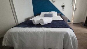 Ein ordentlich bezogenes Bett mit weißblauer Tagesdecke, einer dunkelblauen Zudecke und zwei Kissen.