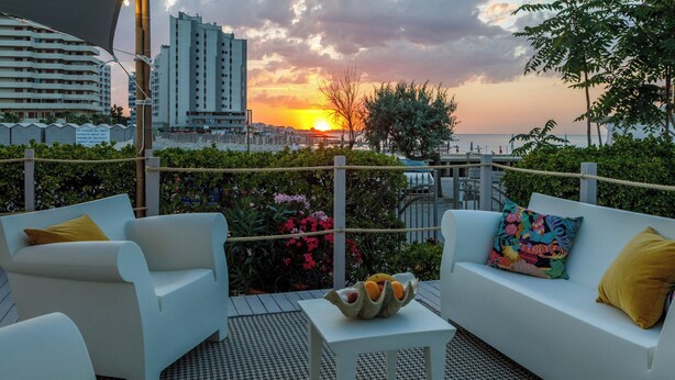 Terraza con sofás blancos y una mesita pequeña, con vistas a un paisaje urbano y al atardecer.