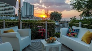 A terrace with white sofas and a small table, overlooking a cityscape and the sunset. - Casetta del Pescatore 4, Emma Villas (Misano Adriatico)