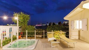 Un área de piscina en la azotea con jacuzzi, sillas de descanso y vistas nocturnas de la ciudad.