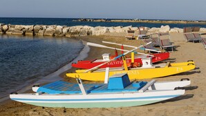 Una playa con varias lanchas de colores, un rompeolas rocoso y sillas de playa.