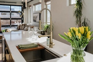 A modern kitchen with a central island, stainless steel sink, and a vase of yellow flowers. - Upscale Retreat in LoHi 4Bd 4.5 Ba, Gym Theatre Rooftop, Near Coors Field (Denver)
