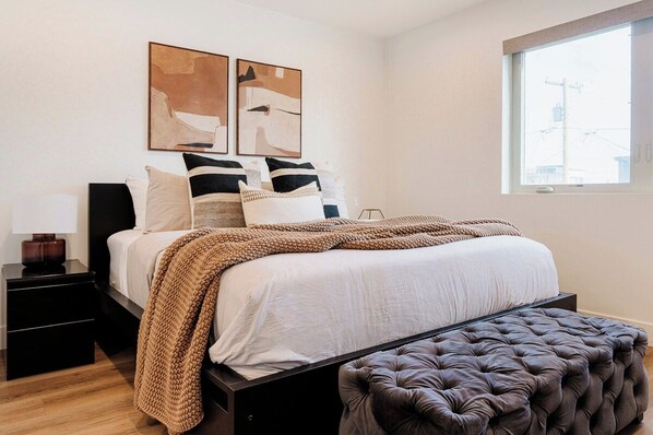 A bedroom with a bed, bedside tables, a window, and abstract wall art. - Upscale Retreat LoHi 4Bd 5Ba | Gym Theatre Rooftop (Denver)