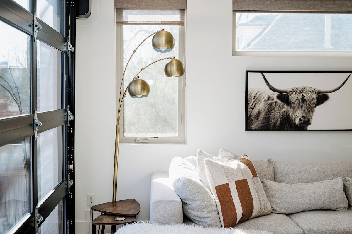 A room with a sofa, a floor lamp, a framed picture of a bull, and a window with blinds.