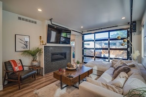 A modern living room with a fireplace, a sofa, a coffee table, and a large window. - Upscale Retreat LoHi 4Bd 5Ba | Gym Theatre Rooftop (Denver)