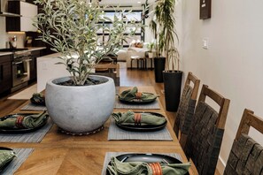 Un coin repas agrémenté d’une grande plante en pot, de chaises en bois et d’une table en bois mise pour le repas.