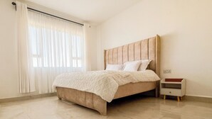 A bedroom with a bed, a nightstand, and a window with curtains. - Spacious & Peaceful Getaway in Imara Daima (Nairobi)