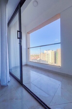 Un balcón con vistas despejadas a un paisaje urbano, una puerta corredera de vidrio y piso de baldosas.