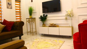 A living room with a brown sofa, a red armchair, a white console table with a flat-screen TV, and decorative plants. - 3 Bedrooms House in a secure and gated estate. (Lagos)