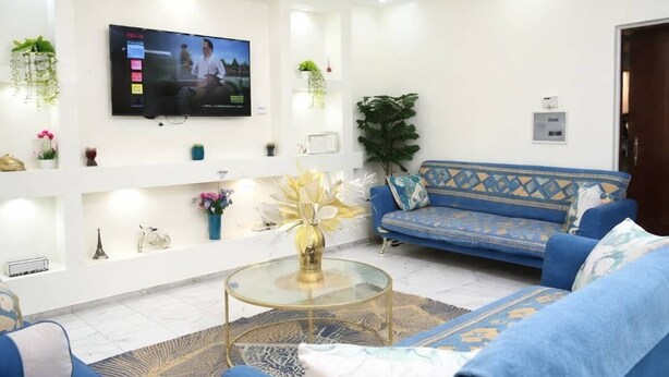 Un salon moderne avec un canapé bleu, une table basse en verre et un téléviseur à écran plat fixé au mur.