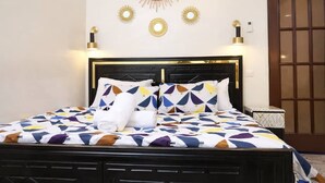 Un lit bien fait, avec une couvre-lit à motifs géométriques, une tête de lit noire et des lampes décoratives fixées au mur.