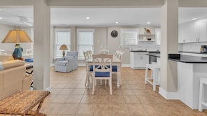 A modern kitchen with white cabinets, a dining area with a white table and chairs, and a living area with a sofa and a lamp. - Boracay Lower - Oceanfront 3 Bedroom, 2 Bathrooms (Kure Beach)