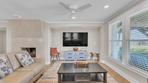 A living room with a beige sofa, a coffee table, a TV, a fireplace, and a ceiling fan. - Boracay Lower - Oceanfront 3 Bedroom, 2 Bathrooms (Kure Beach)